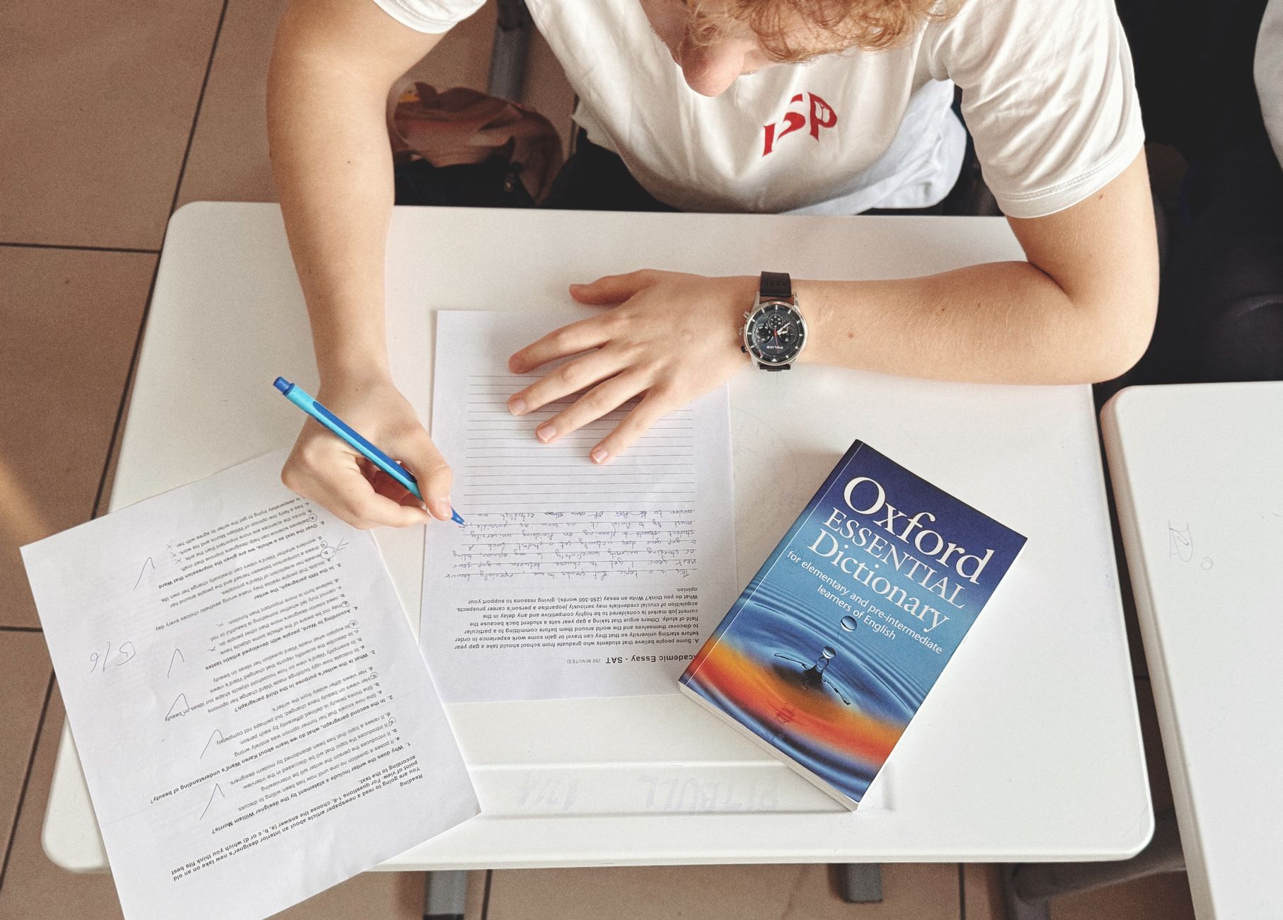 A student writing at a desk with a dictionary