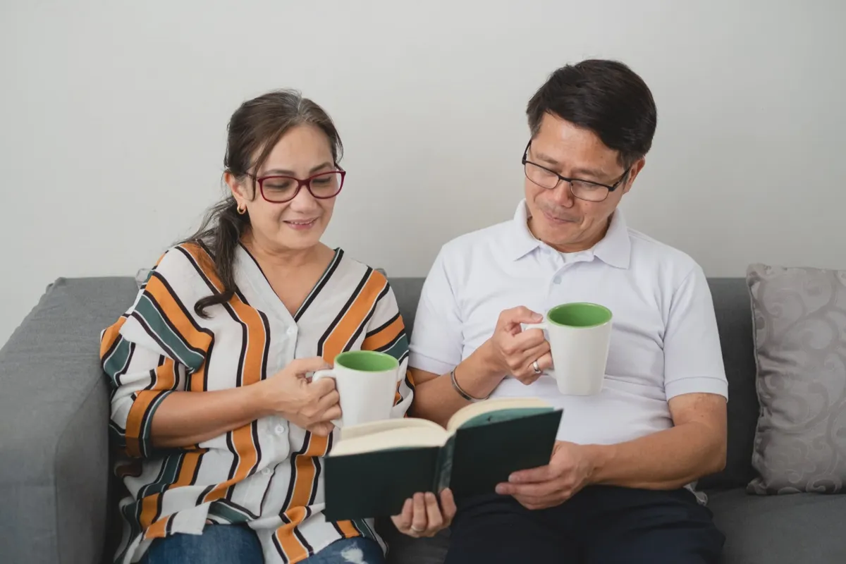 Two language learners sitting comfortably on a couch reading books in English